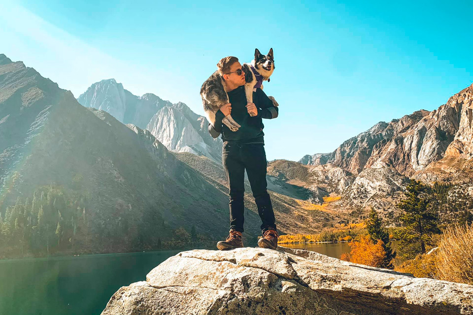 NCC Alum standing on a peak with a dog across his shoulders