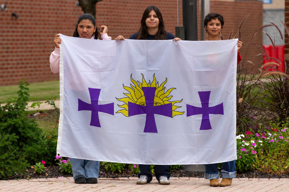 Three female students holding the Hispanic Herotage flag