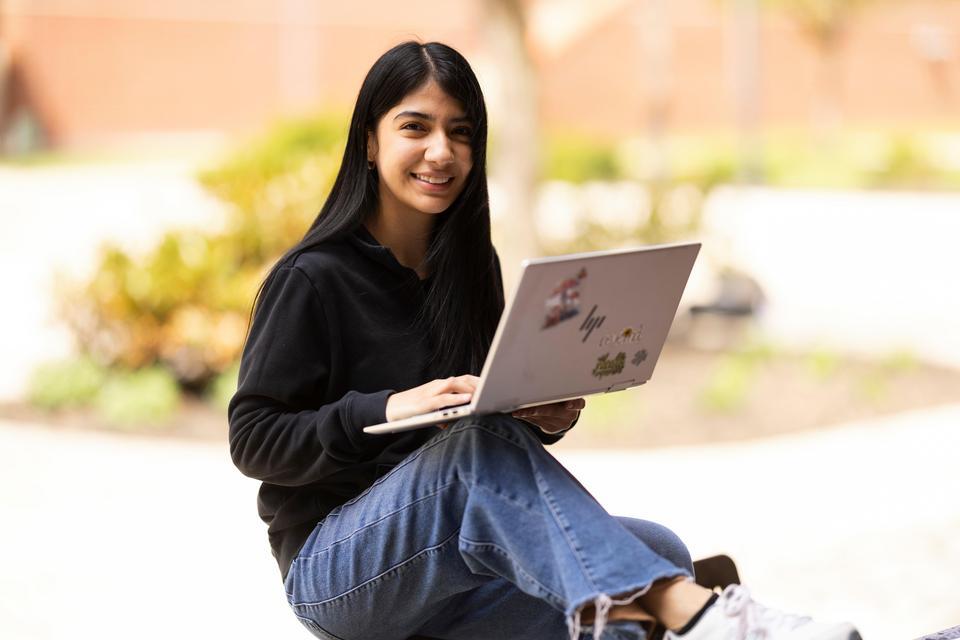 Female student sitting outdoors using a laptop on campus