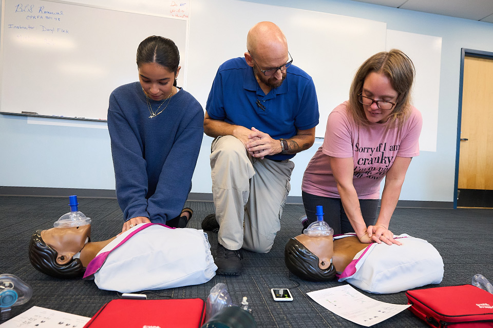Instructor teaching two students on how to perform CPR
