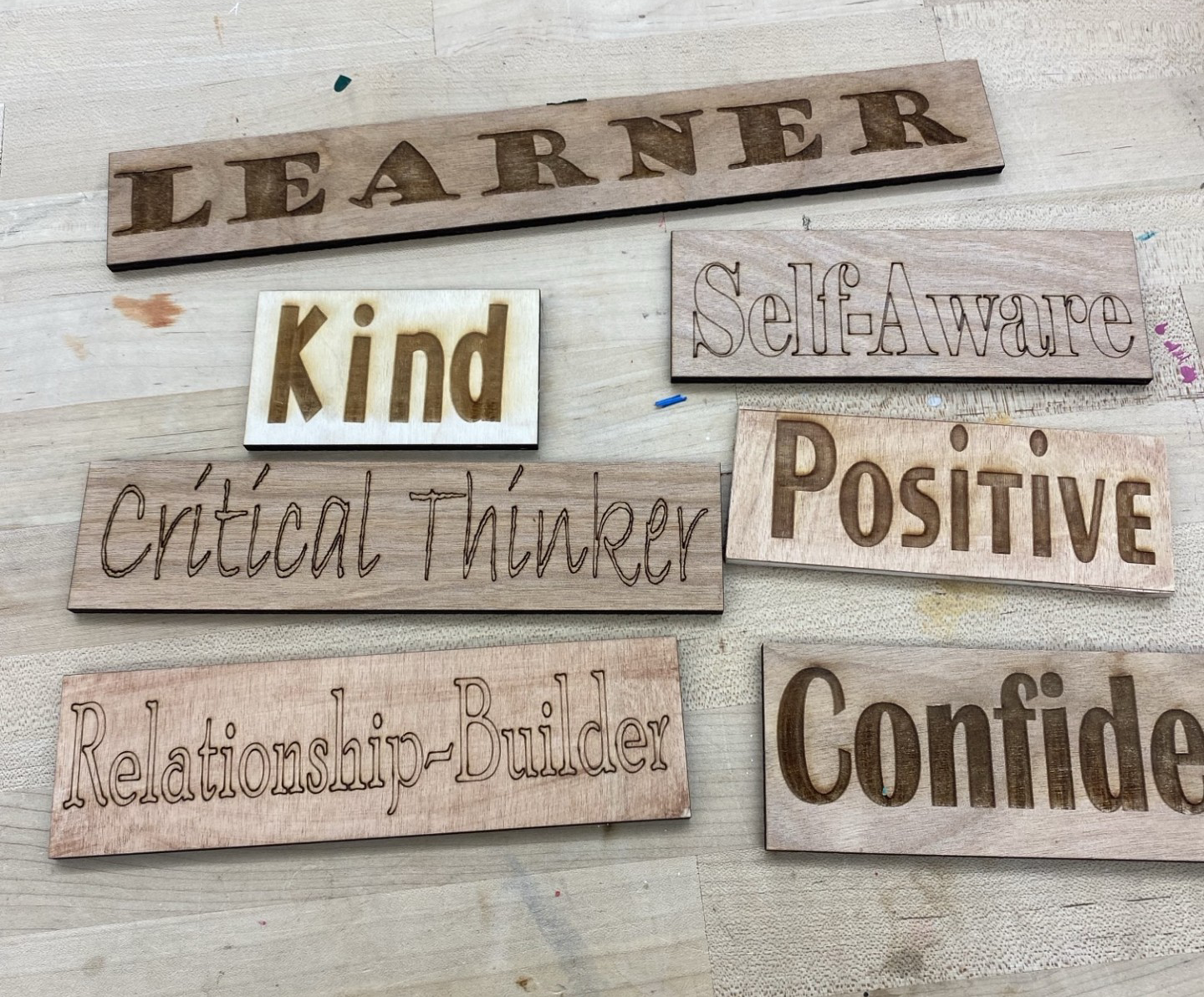Wooden plaques with positive character traits and attributes including "Learner," "Kind," "Self-Aware," "Positive," "Critical Thinker," "Relationship-Builder," and "Confident."